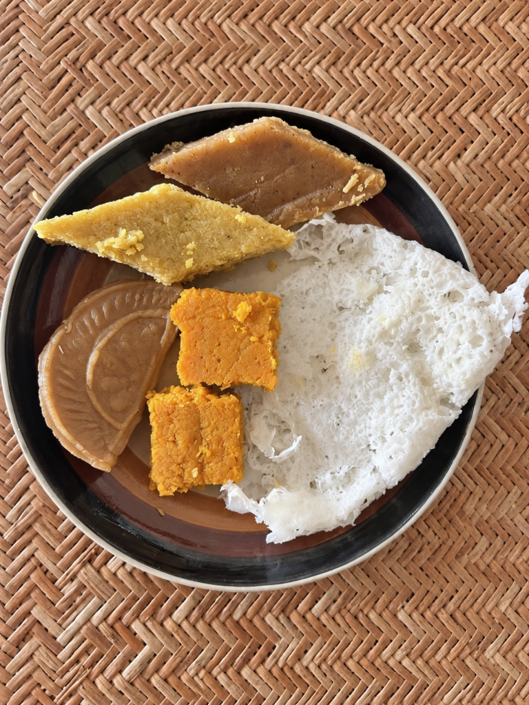 Paula’s homemade Shab-e-Barat assortment—egg-semolina barfi, carrot barfi, boot barfi, chandrapuli and a delicate white sweet—served on a round plate over woven cane.